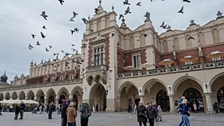 Gołębie przelatują nad głowami, a ludzie spacerują po Rynku Głównym w niedzielę, 9 listopada 2025 roku, na Starym Mieście w Krakowie.