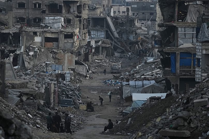 Palestinianos caminham entre edifícios destruídos pelas operações aéreas e terrestres israelitas na Cidade de Gaza, 6 de janeiro de 2026