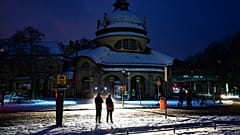 Passanten stehen im Licht einer Feuerwehrhilfsstelle in Berlin, Deutschland, Samstag, 3. Januar 2025, während eines Stromausfalls im Südwesten Berlins nach einem Brand auf einer Brücke.