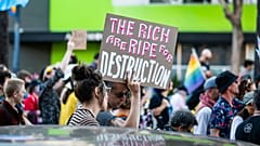 Ein Demonstrant hält ein Schild hoch. „Die Reichen sind reif für Zerstörung.“