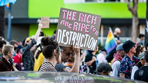 A protestor holding a sign reading "The rich are ripe for destruction". 