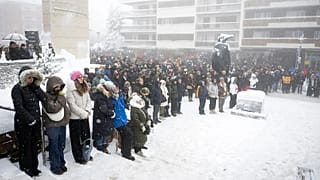 People observe a minute of silence as they watch the official commemorative ceremony on a screen in Martigny, 9 January, 2026