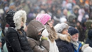 Des personnes observent une minute de silence en regardant la cérémonie commémorative officielle sur un écran à Martigny, le 9 janvier 2026.