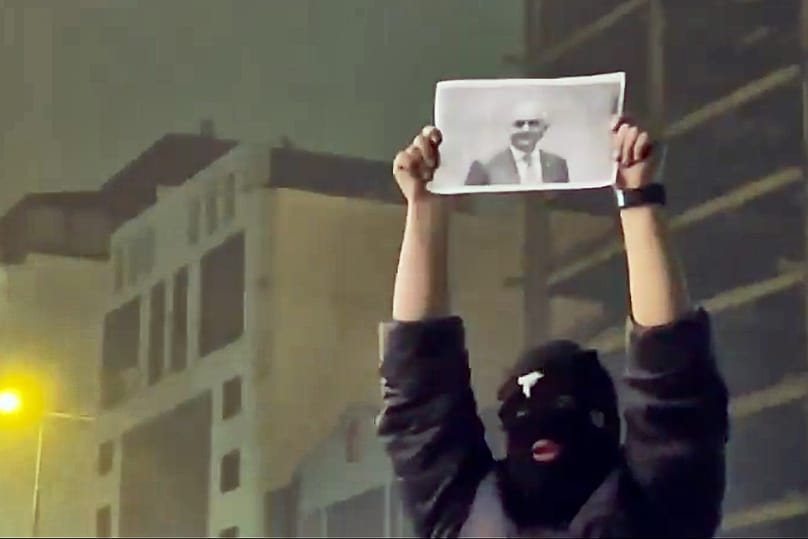 A masked demonstrator holds a picture of Iran's Crown Prince Reza Pahlavi during a protest in Tehran, Iran, Friday, January. 9, 2026