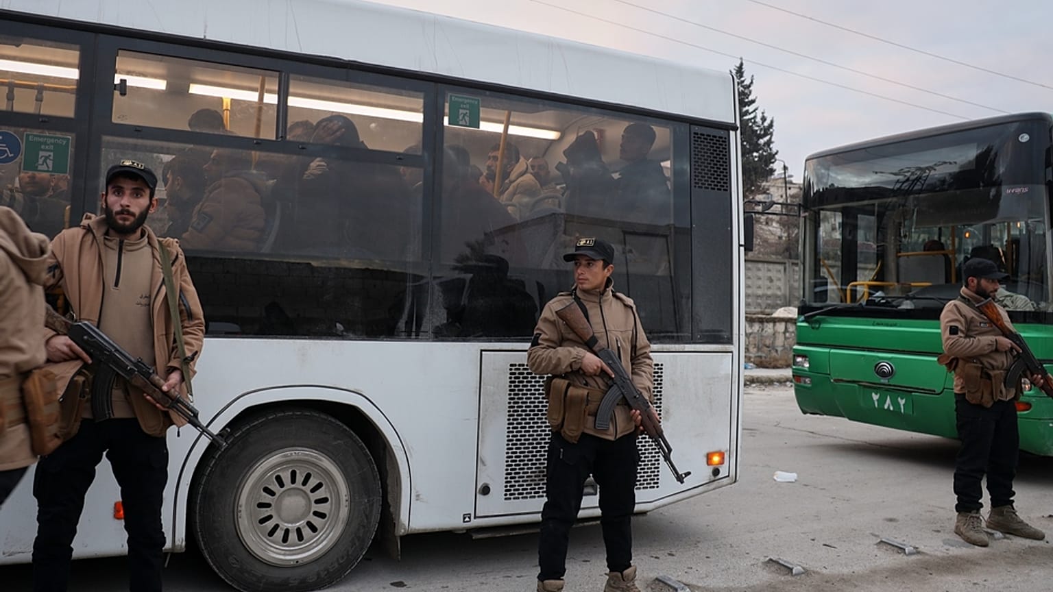 عناصر من الأمن السوري يقفون بجانب حافلات تقل مقاتلين استسلموا خلال اشتباكات بين القوات الحكومية وقوات سوريا الديمقراطية ذات الغالبية الكردية في مدينة حلب شمالي سوريا