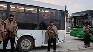 عناصر من الأمن السوري يقفون بجانب حافلات تقل مقاتلين استسلموا خلال اشتباكات بين القوات الحكومية وقوات سوريا الديمقراطية ذات الغالبية الكردية في مدينة حلب شمالي سوريا