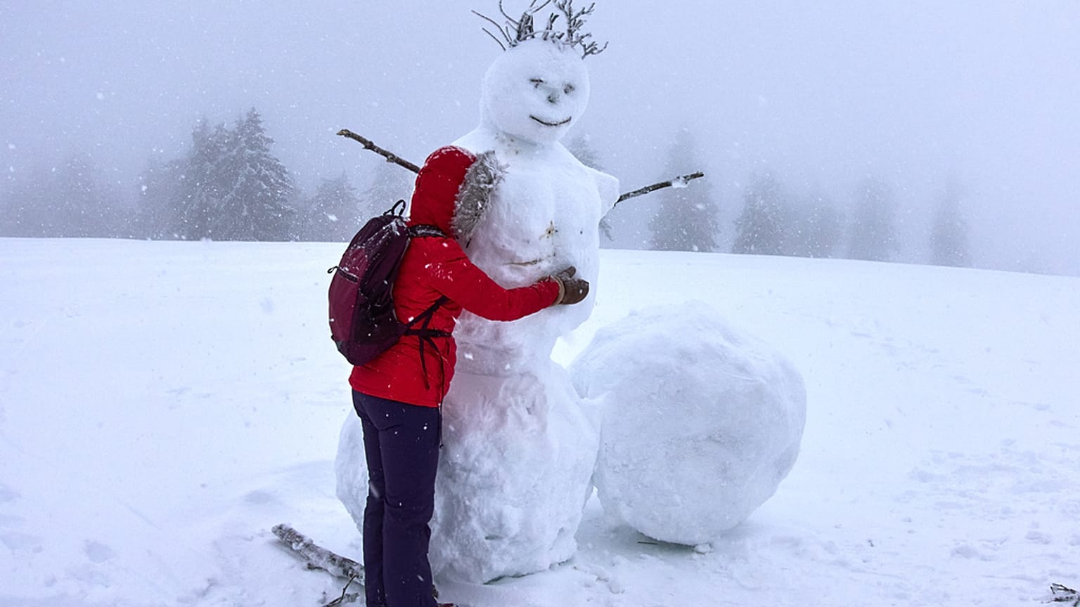 Frau umarmt einen Schneemann am Feldberg im Taunus