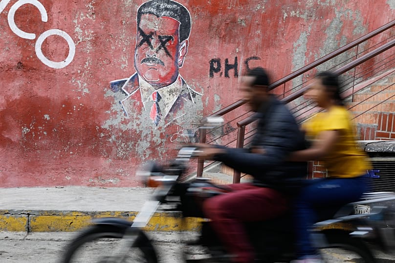 A motorcyclist rides past graffiti depicting former Venezuelan President Nicolás Maduro in Caracas, 11 January, 2026