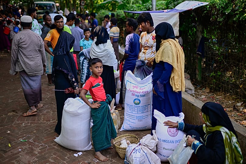 Rohingya refugees wait with their collected food rations before taking them home in the Rohingya refugee camp in Cox's Bazar, Bangladesh, Tuesday, Nov. 25, 2025.