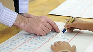 Lehrer Jeff Parker hilft einem Schüler beim Üben des Schreibens von Buchstaben des Alphabets während des Unterrichts am Montag, dem 29. September 2014.