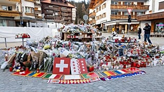 Targhe con bandiere che rappresentano Svizzera, Romania, Italia, Portogallo, Belgio, Francia e Turchia insieme a fiori e candele per onorare le vittime dell'incendio 