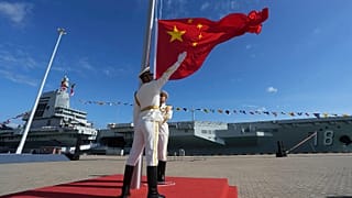 Membros da guarda de honra hasteiam a bandeira nacional chinesa durante a entrada em serviço do terceiro porta-aviões da China na província de Hainan, 5 de novembro de 2025