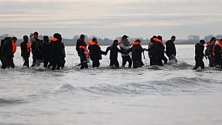 Migrants push a small boat in an attempt to reach the UK, 6 November, 2025