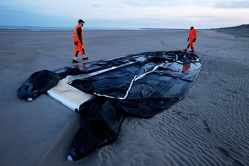 Town employees walk next to an inflatable boat punctured on the beach of Gravelines, 22 December, 2025