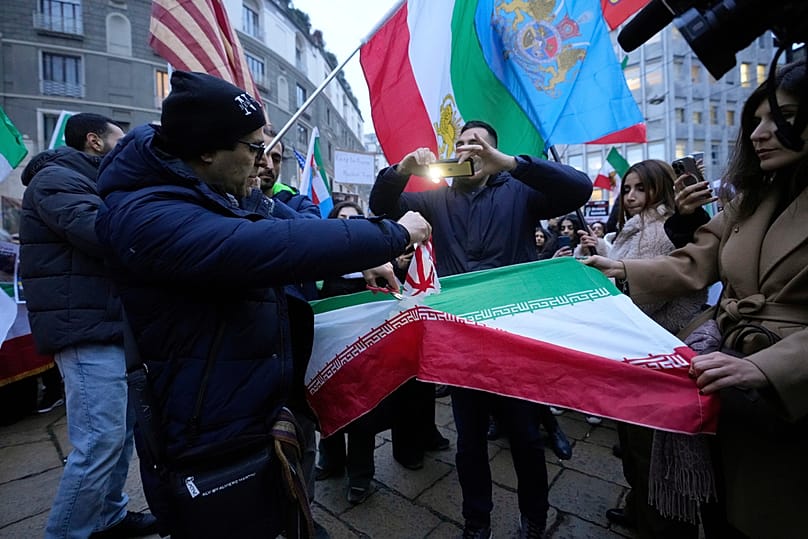 متظاهرون إيرانيون يقطعون علم الدولة الإسلامية خلال تظاهرة دعم للاحتجاجات الشعبية ضد الحكومة أمام القنصلية الأمريكية في ميلانو، في 13 يناير 2026.