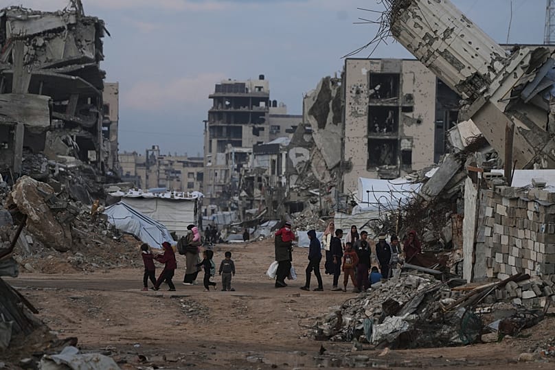 Palestinians walk amid buildings destroyed by Israeli air and ground operations in Gaza City, 14 January, 2026