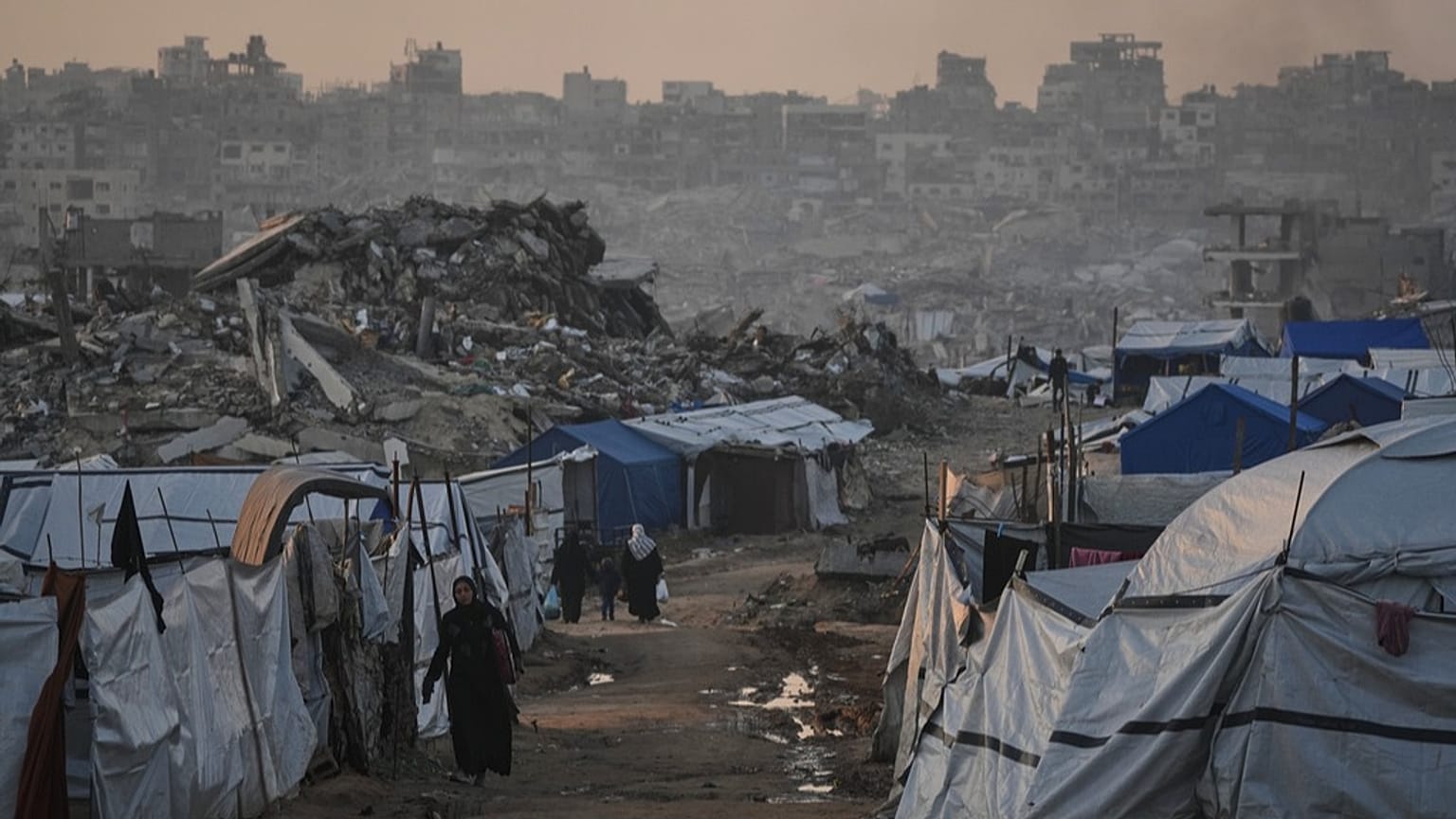 فلسطينيون يمرّون قرب خيام تمّ تشييدها بين مبانٍ دمّرتها الحرب الإسرائيلية على غزة، بتاريخ 6 يناير 2026.