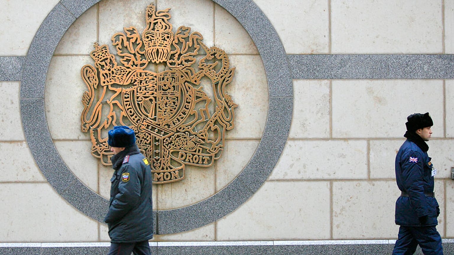  يسير شرطي روسي بمحاذاة جدار (يسارًا) بينما يحرس ضابط أمن بريطاني (يمينًا) مبنى السفارة البريطانية في موسكو