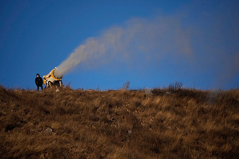 A person works at a snow making machine on a hill overlooking cross-country skiing practice before the 2022 Winter Olympics in China. 