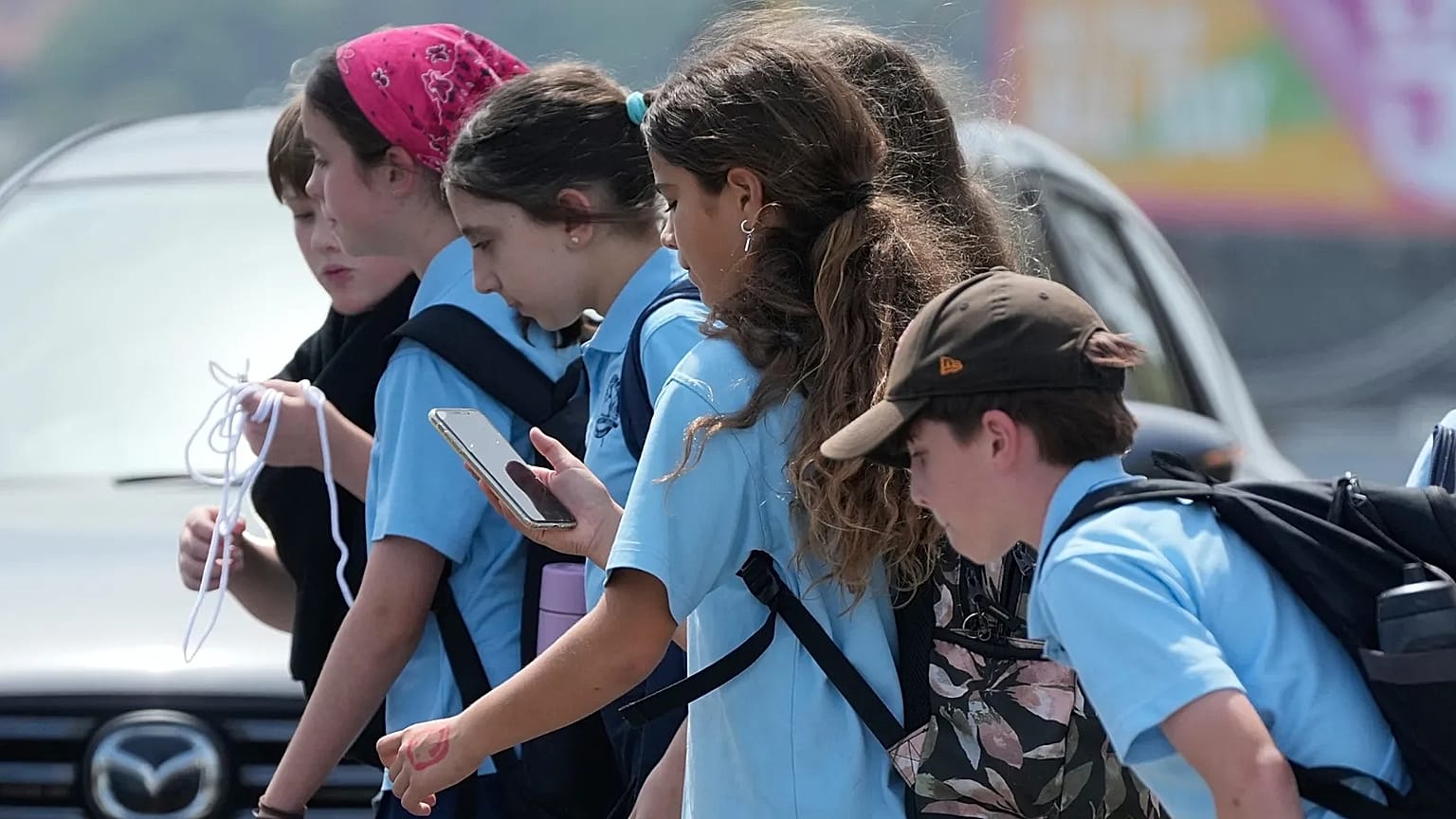 A school girl uses her phone as she walks with a group of kids in Sydney, Monday, Dec. 8, 2025. 