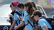Une écolière utilise son téléphone en marchant avec un groupe d'enfants à Sydney, lundi 8 décembre 2025.