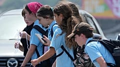Sydney, Montag, der achte Dezember 2025: Ein Schulmädchen schaut auf ihr Handy und geht mit einer Kindergruppe.
