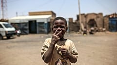 طفل سوداني يشير إلى الكاميرا ليطلب سيجارة، خارج منزله في إزبا. (صورة من وكالة أسوشيتد برس/مصعب الشامي)