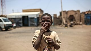 طفل سوداني يشير إلى الكاميرا ليطلب سيجارة، خارج منزله في إزبا. (صورة من وكالة أسوشيتد برس/مصعب الشامي)