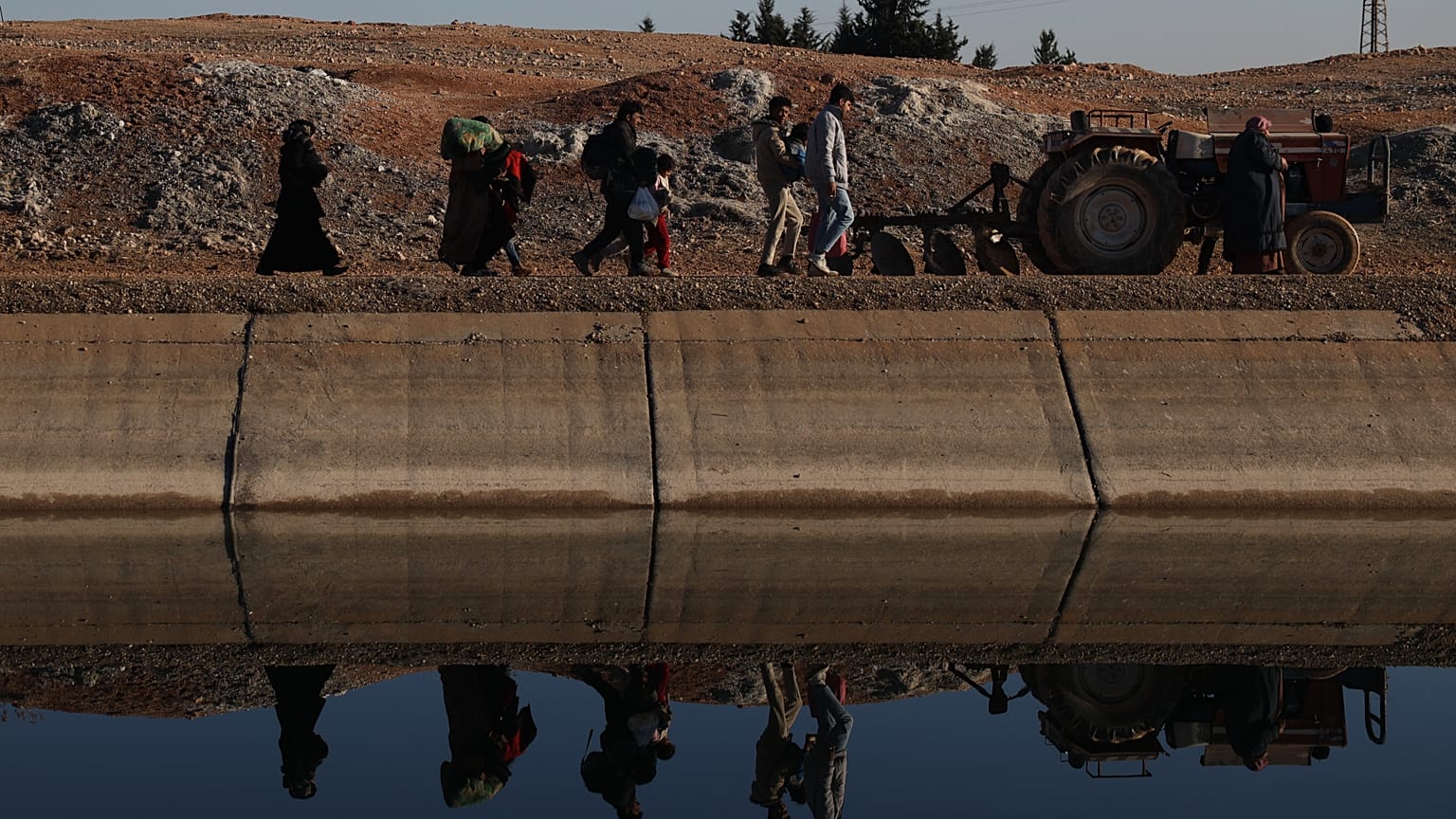 Suriye'de yerinden edilmiş kişiler, Halep kırsalının doğusunda Cerirat el İmam köyü yakınlarındaki bir nehir geçidinden karşıya geçmek için yürüyor, 15 Ocak 2026.