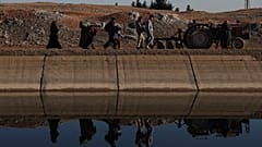 Suriye'de yerinden edilmiş kişiler, Halep kırsalının doğusunda Cerirat el İmam köyü yakınlarındaki bir nehir geçidinden karşıya geçmek için yürüyor, 15 Ocak 2026.