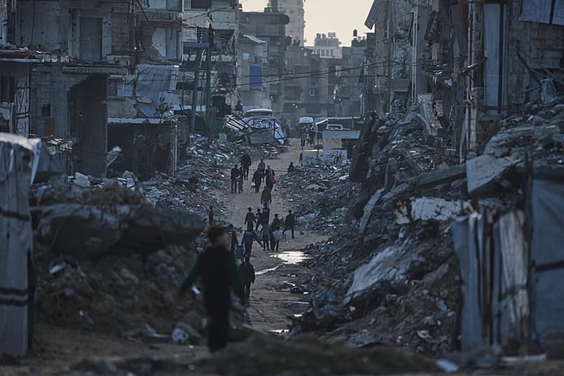 Palestinians walk amid buildings destroyed by Israeli air and ground operations in Gaza City, 15 January, 2026