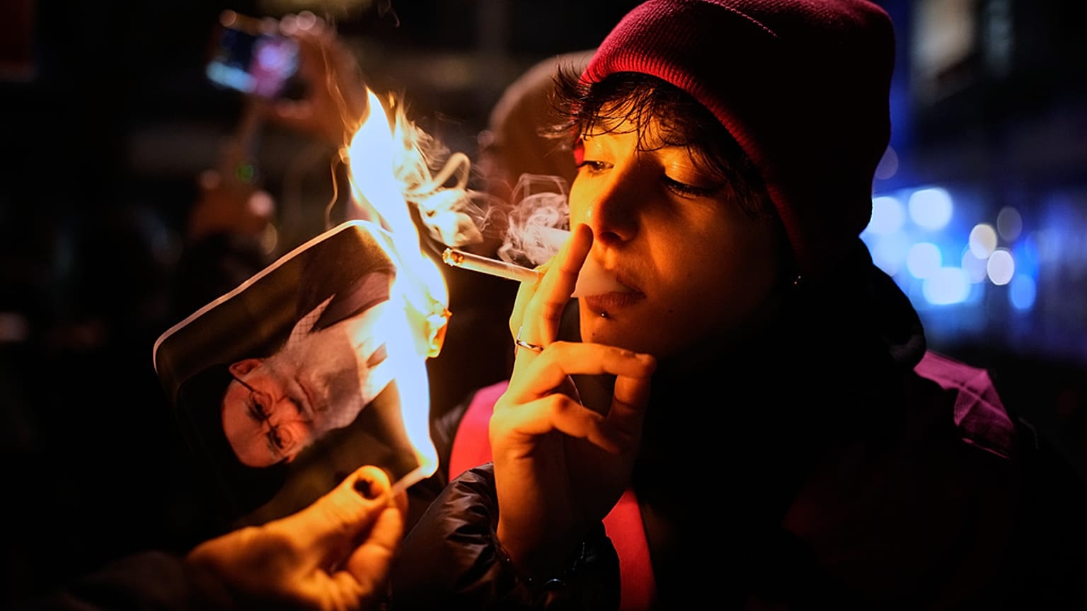 متظاهر في ألمانيا يشعل سيجارته بملصق للمرشد الإيراني علي خامنئي تضامناً مع الاحتجاجات في إيران