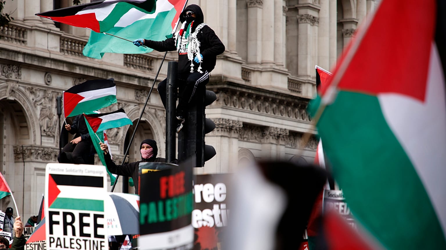 المتظاهرون يرفعون الأعلام واللافتات أثناء وقوفهم على إشارات المرور قرب داونينغ ستريت خلال مظاهرة مؤيدة للفلسطينيين في لندن