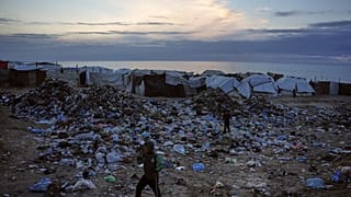 أطفال يسيرون فوق أكوام من النفايات في مخيم خيام مؤقت للنازحين الفلسطينيين على أحد شواطئ مدينة دير البلح وسط قطاع غزة، الجمعة 16 جانفي/يناير 2026.