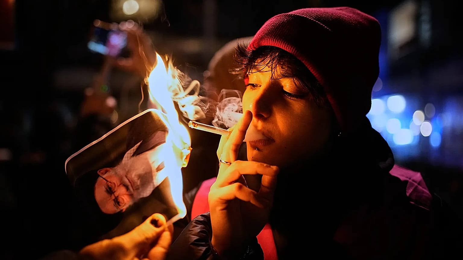 A protester smokes a cigarette after lighting it off a burning poster of Iran's Supreme Leader Ayatollah Ali Khamenei during a demonstration in Berlin, 14 January, 2026