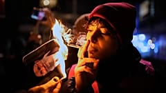 Bir protestocu, Berlin'deki bir gösteri sırasında İran'ın Dini Lideri Ayetullah Ali Hamaney'in yanan posterini yaktıktan sonra sigara içiyor, 14 Ocak 2026
