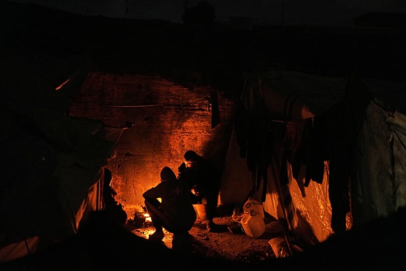 Displaced Palestinians cook and warm themselves around a fire at a tent camp in Gaza City, 18 January, 2026