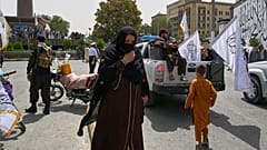 زنی با ماسک صورت، در میان جمعیت جنگجویان طالبان و هوادارانشان، در جریان مراسم جشن چهارمین سالگرد خروج نیروهای آمریکا و آغاز حاکمیت طالبان، جمعه ۱۵ اوت ۲۰۲۵
