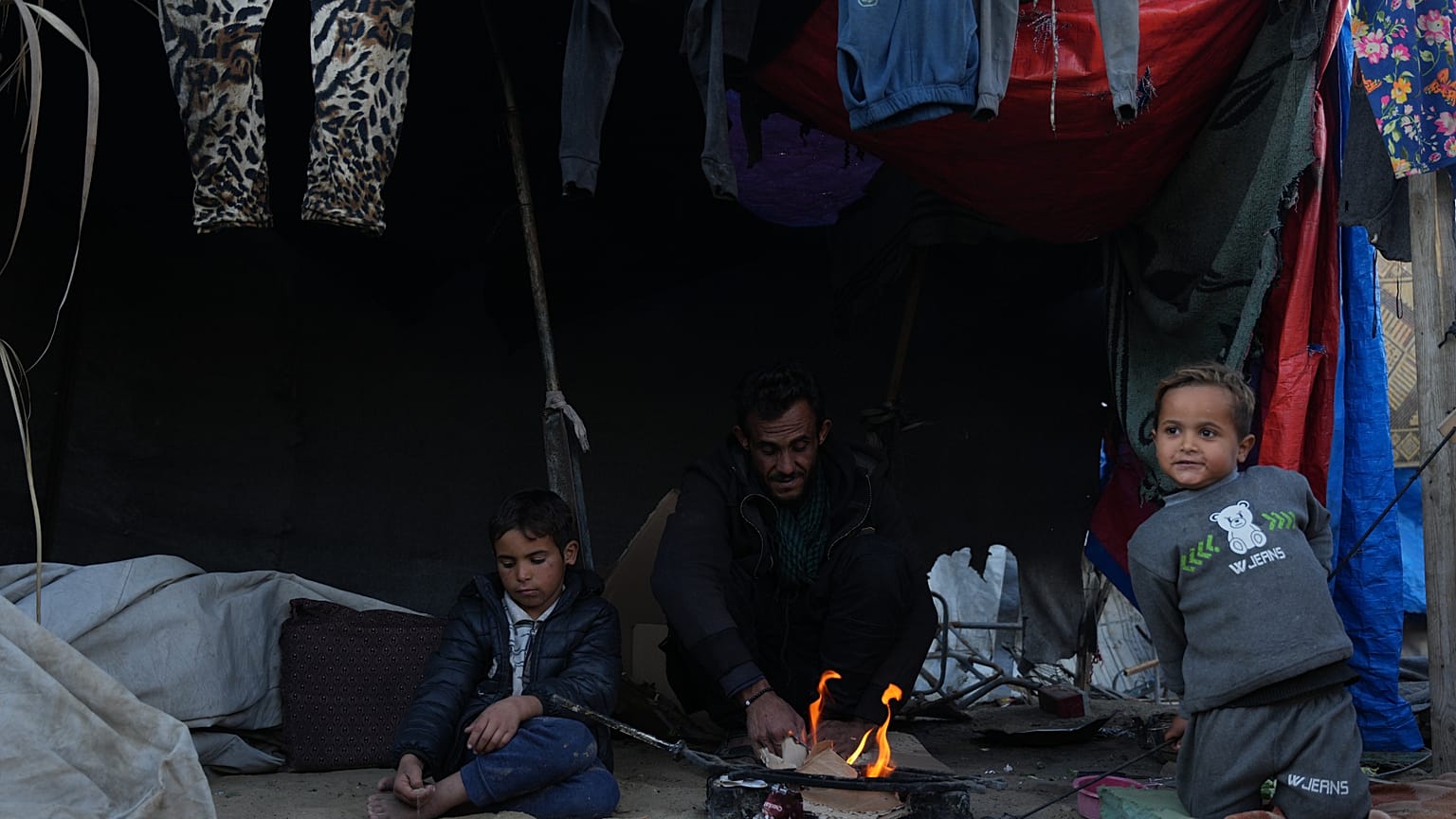 نازح فلسطيني يجلس إلى جانب النار مع أطفاله قرب خيمتهم في دير البلح، وسط قطاع غزة، السبت 17 كانون الثاني/يناير 2026. 