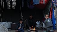 نازح فلسطيني يجلس إلى جانب النار مع أطفاله قرب خيمتهم في دير البلح، وسط قطاع غزة، السبت 17 كانون الثاني/يناير 2026. 