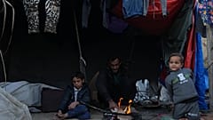 نازح فلسطيني يجلس إلى جانب النار مع أطفاله قرب خيمتهم في دير البلح، وسط قطاع غزة، السبت 17 كانون الثاني/يناير 2026. 