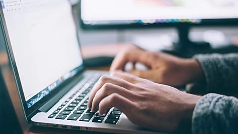 A close-up shot of a man typing on a laptop.