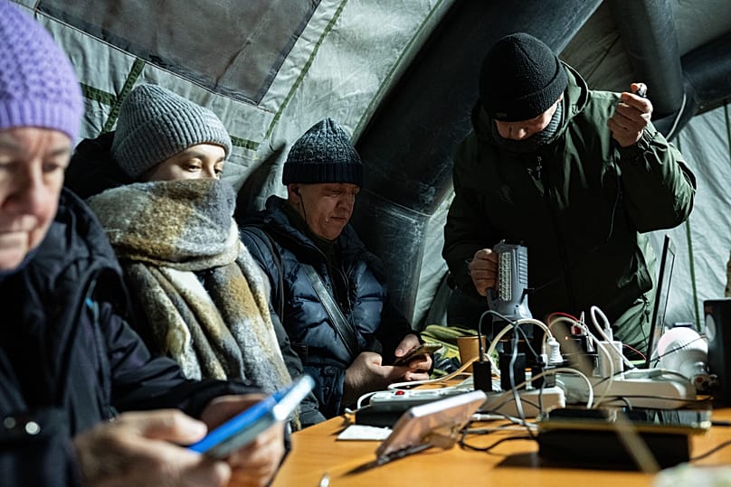 Pessoas aquecem-se e carregam os seus dispositivos móveis durante um corte de energia causado pelos ataques aéreos regulares da Rússia ao setor energético do país, em Kiev