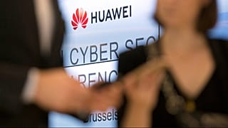 Two people look at their cellphones in front of the Huawei logo during a DigitALL lunch talk in Brussels, Tuesday, May 21, 2019.