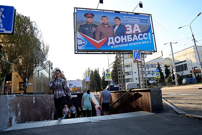 People walk out from an underground crossing decorated with a United Russia party poster in Donetsk, 7 September, 2023