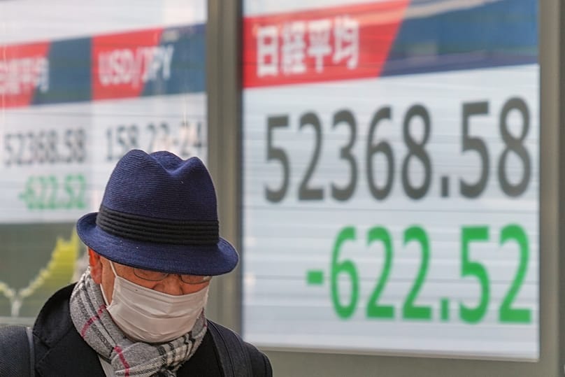 A person walks in Tokyo as the screen shows the Nikkei falling, 21 January 2026