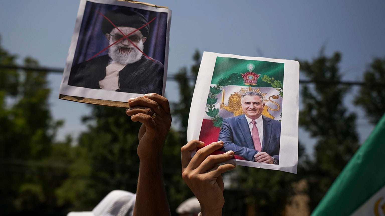 متظاهر يحمل ملصقاً لولي العهد الإيراني المنفي رضا بهلوي (يمين الصورة)، وملصقاً مشوهاً للمرشد الأعلى الإيراني آية الله علي خامنئي، خلال مسيرة دعماً للاحتجاجات المناهضة للحكومة 