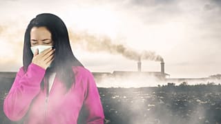 امرأة تضع كمامة فيما يتصاعد الدخان من المصانع في الخلفية