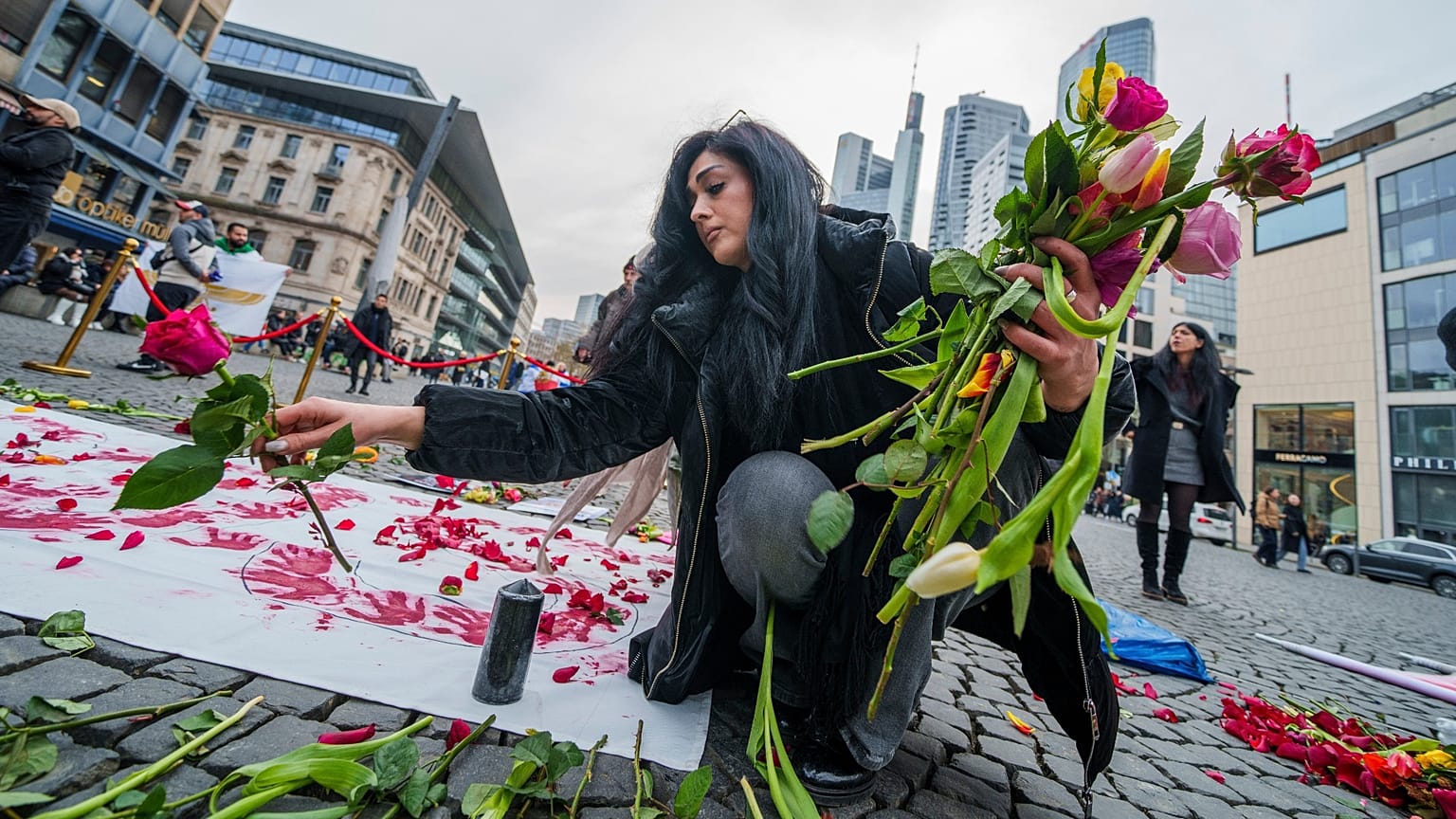 زنی در حال قرار دادن گل در مکانی نمادین برای گرامیداشت جان باختگان اعتراضات ایران در جریان تظاهرات حامیان معرتضان ایرانی در شهر کلن آلمان