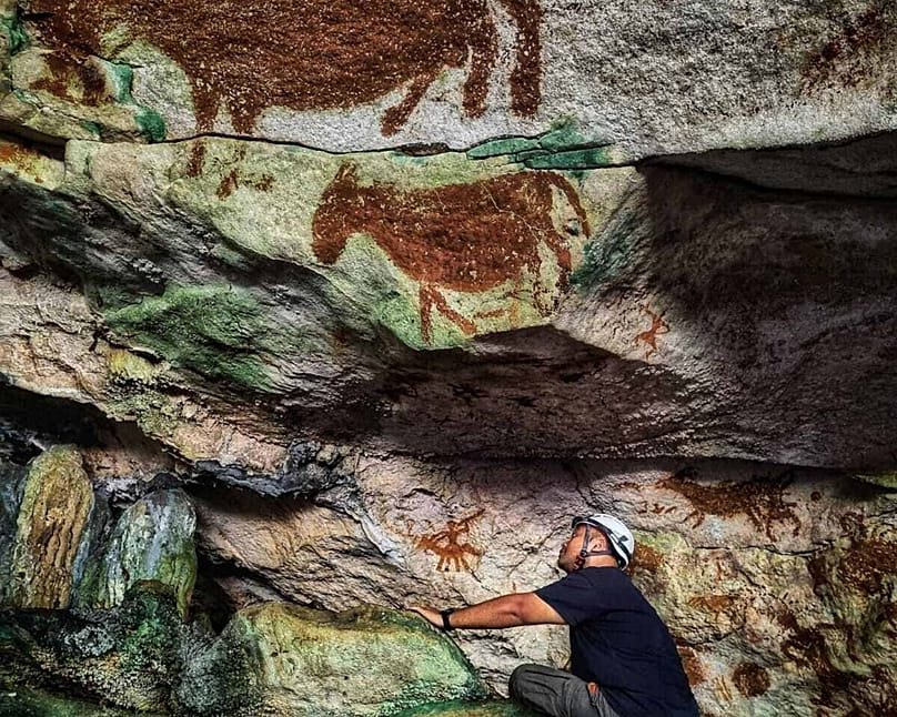 This image provided by Maxime Aubert shows scientist Shinatria Adhityatama studying cave art found in Sulawesi, Indonesia.